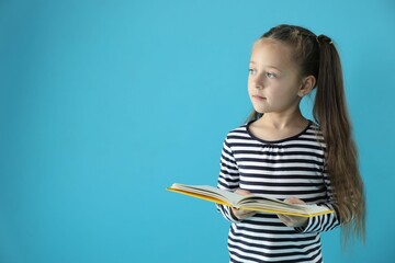 Learning alphabet. Little girl with book on light blue background, space for text