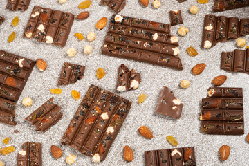 Broken chocolate pieces with nuts and raisins on a stone background top view