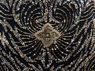 Golden sequin and bead ornament on black mesh fabric. Element of an evening dress.