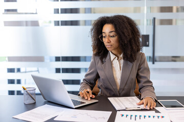 Young african american female accountant, financial expert sitting in office at desk and working on...