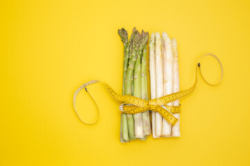 bundles of white and green asparagus secured with a measuring tape on a yellow background. Weight loss concept.