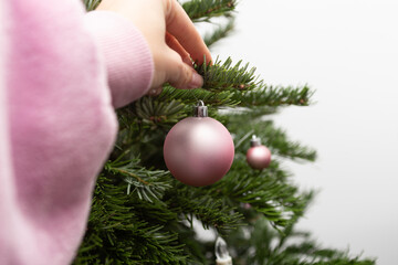 a woman's hand hangs a pink Christmas ball on a Christmas tree