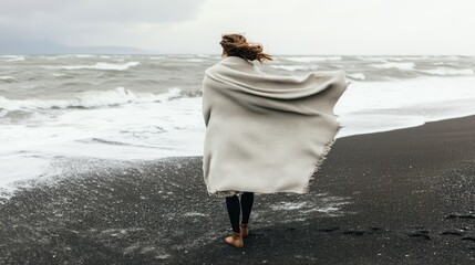 Solitary Figure Wrapped in Blanket Facing Stormy Sea on Windy Beach Day