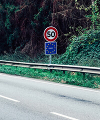 Speed limit sign indicating 50 km/h on a rural road in France surrounded by greenery and trees during daytime