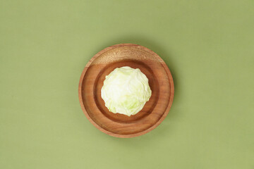 Green cabbage on a wooden plate, isolated against a green background, top view