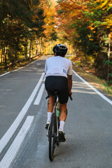Fototapeta premium Cyclist rides road bike through scenic autumn forest. Stunning fall foliage creates a vibrant backdrop. Perfect for active lifestyle, travel, and sports themes.