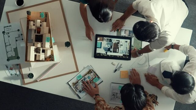 Time lapse of designer looking at model while discussing about building. Top view of architect engineer explaining idea while talking and writing blue print scattering at meeting table. Alimentation.
