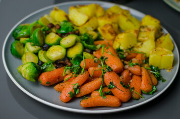 
Vegetables for roast dinner - sauteed carrots with garlic, butter and anise, broccoli with pancetta, roast potatoes in duck grease, on a grey table, Christmas roast ideas