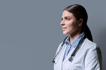Profile view of positive young female doctor with stethoscope on gray background