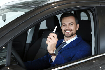 Happy salesman holding key inside new black car in salon