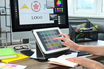 Designer working on tablet at wooden table indoors, closeup