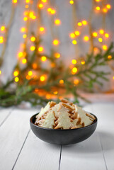 The black deep plate is filled with shortbread Christmas cookies. There are yellow lights and a branch of a Christmas tree in the background.