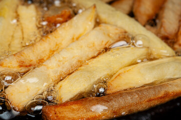 Potato fries sizzle and bubble in hot oil, becoming crispy and golden