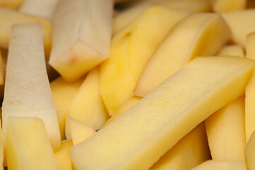 A close-up view of freshly cut, pale yellow potato wedges piled together