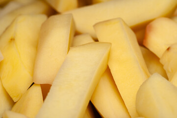 A close-up view of freshly cut, pale yellow potato wedges piled together