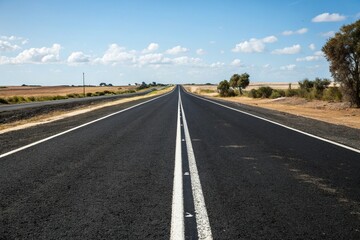 Fototapeta premium Straight black asphalt road with white dividing lines on a sunny day, road, roads, white lines