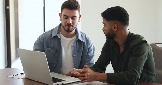 Two busy young Middle Eastern business partners cooperating on project, working at laptop at office workplace together, talking, discussing startup management, teamwork