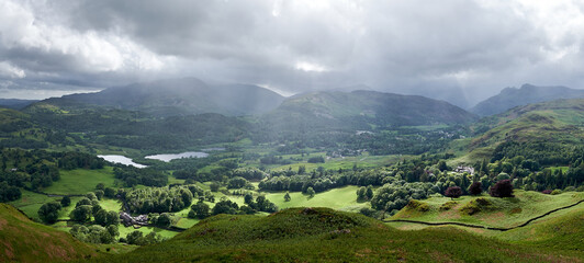 Panorama of light breaking through clouds onto farm land below Loughrigg Fell, Lake District, UK