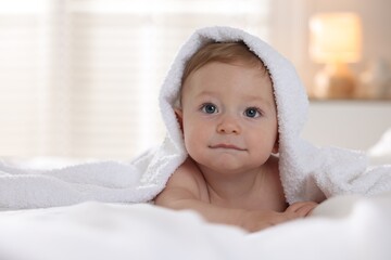 Cute baby under terry towel lying on bed at home