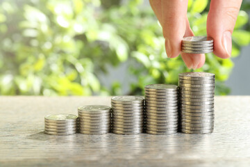 Salary concept. Woman putting coins on stack at grey table, closeup