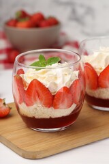 Tasty trifle dessert. Sponge cake, strawberries, jam and whipped cream in glasses on white table, closeup