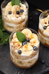 Tasty trifle dessert. Sponge cake, blueberries, banana and whipped cream in glasses on table, closeup