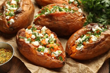 Tasty cooked sweet potatoes with feta cheese, green onion and parsley on table, closeup