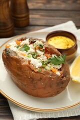 Tasty baked sweet potato with feta cheese, parsley and sauce on wooden table, closeup