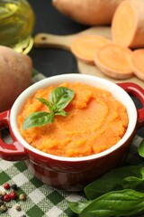 Tasty mashed sweet potato with basil in, fresh vegetables and spices on table, closeup