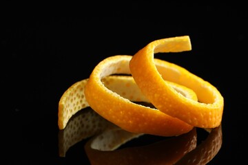 One fresh orange peel on black mirror surface, closeup
