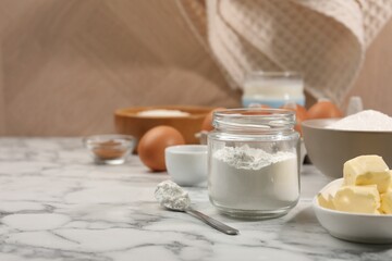 Baking powder in jar and other products on white marble table, closeup. Space for text