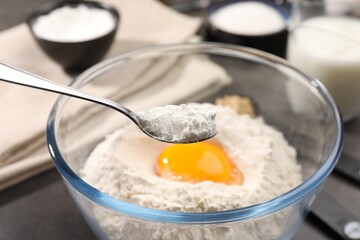 Taking baking powder from bowl with spoon at grey table, closeup