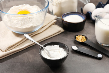 Baking powder and spoon in bowl on grey textured table