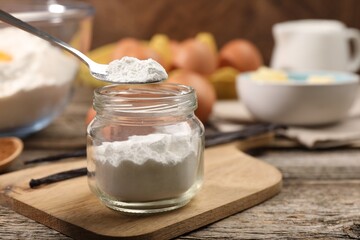 Taking baking powder from jar with spoon at wooden table, closeup