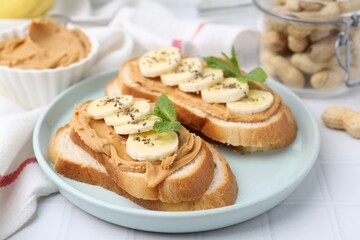 Tasty sandwiches with peanut butter, banana, chia seeds and mint on white table, closeup