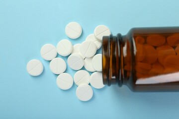 Bottle of antibiotic pills on light blue background, top view