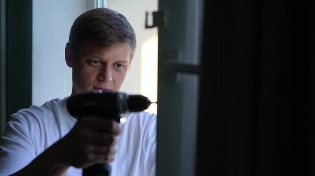 Focused handyman installing winter insulation on window using cordless drill, ensuring energy efficiency and warmth during cold season. Concept of plastic window maintenance. Shooting in slow motion.