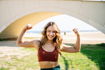 Young sporty woman showing muscles under white bridge