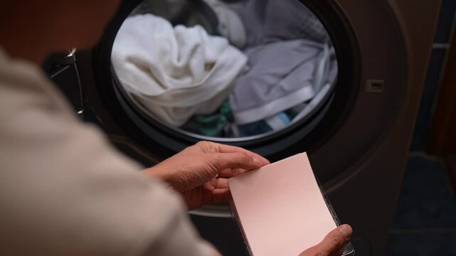 Housekeeper placing white laundry detergent sheet, preparing to load washing machine with dirty clothes, offering modern and convenient approach to laundry. Concept of easy housekeeping domestic life.