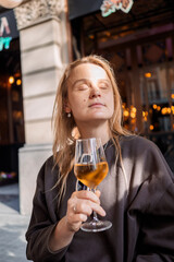 Caucasian woman with blond hair enjoying a glass of white wine outside a cafe in warm sunlight