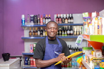A cheerful shopkeeper stands with a clipboard in a colourful grocery store, surrounded by various products. His friendly demeanor adds warmth to the bustling retail environment.