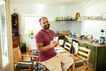 Middle-aged man using smartphone in modern kitchen
