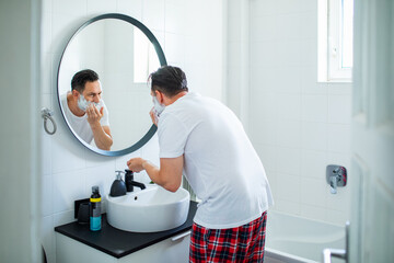 Man shaving in front of bathroom mirror with shaving foam