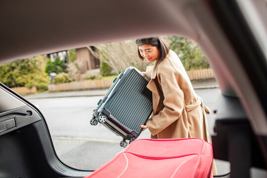 Asian woman packing luggage into car trunk for travel or moving