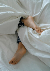 The feet of a small child in a parent's bed on white sheets rolled in a white blanket  
