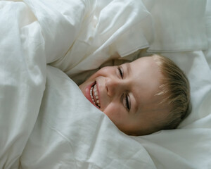 a little blond-haired boy in blue pajamas in his parents' bed lounging in the white sheets