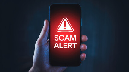A phone with a red alert on it. The alert is for a scam. The person holding the phone is likely trying to warn others about the scam