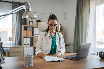 woman doctor signature patient file on clipboard near laptop on desk
