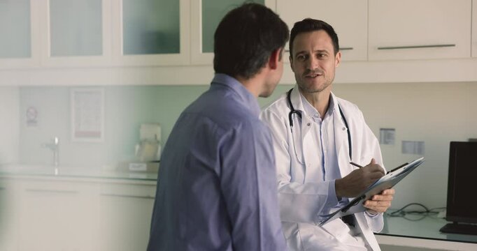 Middle-aged Hispanic general practitioner listening patient health complaints during his visit in clinic, recording relevant information in medical record. Health-care, medicine, professional medicare