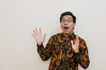 A shocked Southeast Asian man wearing batik shirt and glasses isolated over white background, Positive person, for an advertisement.